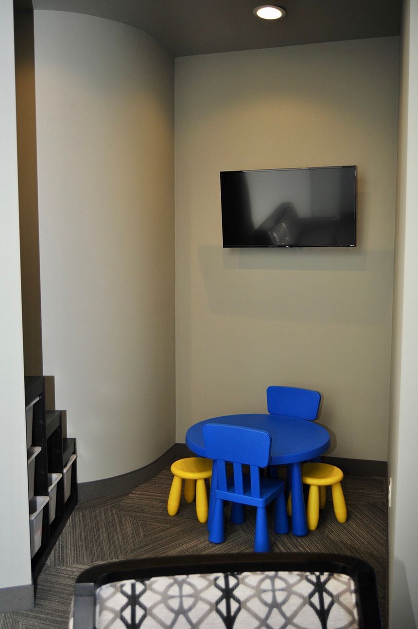 Small kids’ play area with blue and yellow stools under a wall-mounted TV in a recessed corner