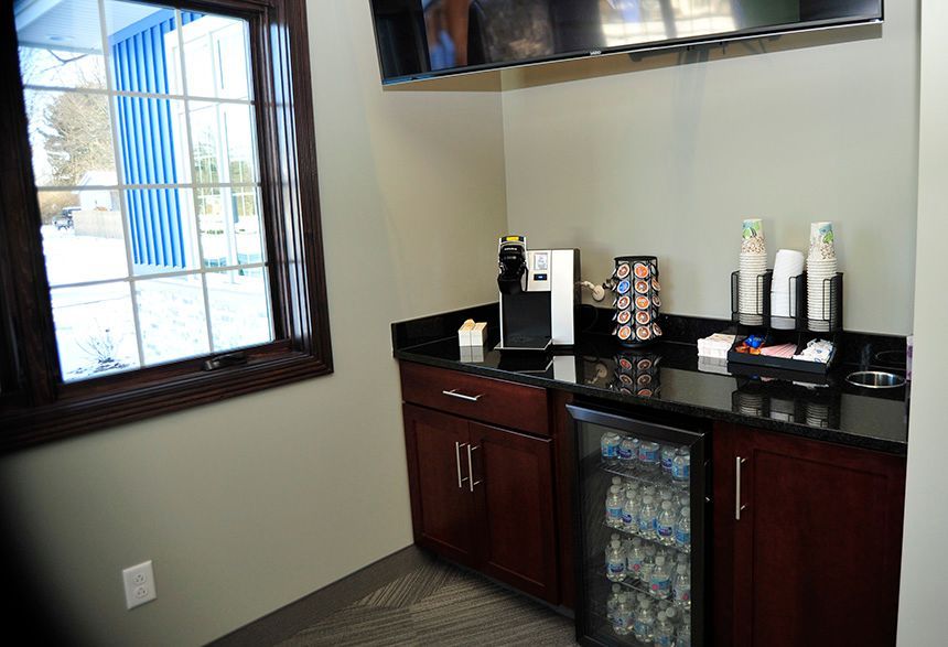 Coffee station with dark wood cabinets, countertop appliances, and a window beside a wall-mounted TV.