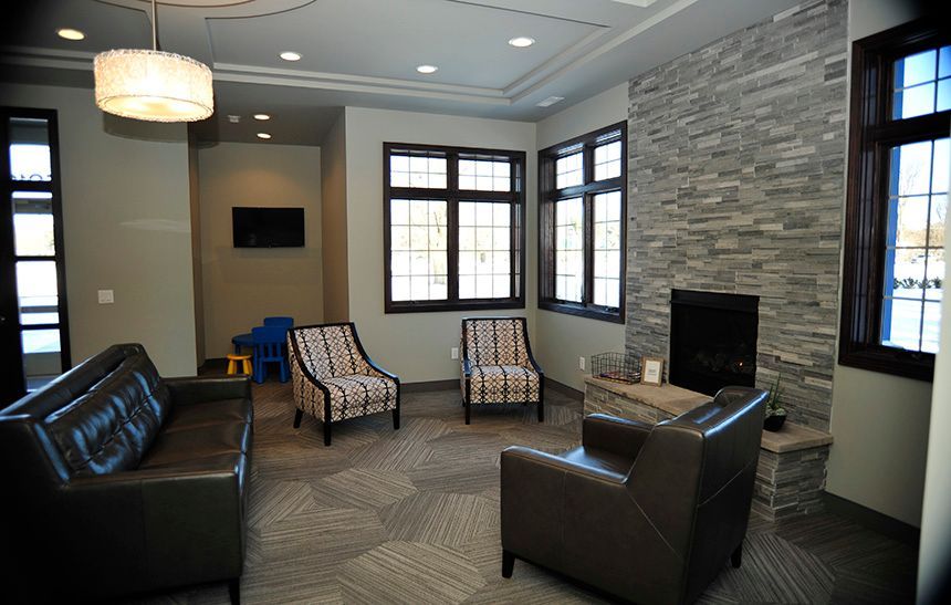 Modern waiting room with black leather sofa, two chairs, windows, and a stone fireplace