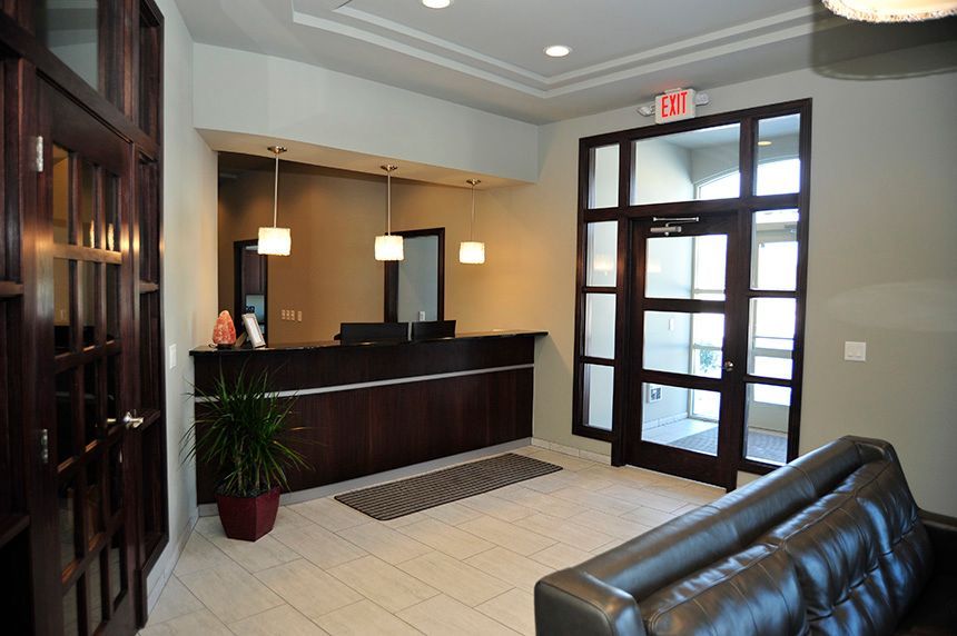 Lobby reception desk with dark wood counter, glass doors, and a leather sofa in a modern office entryway