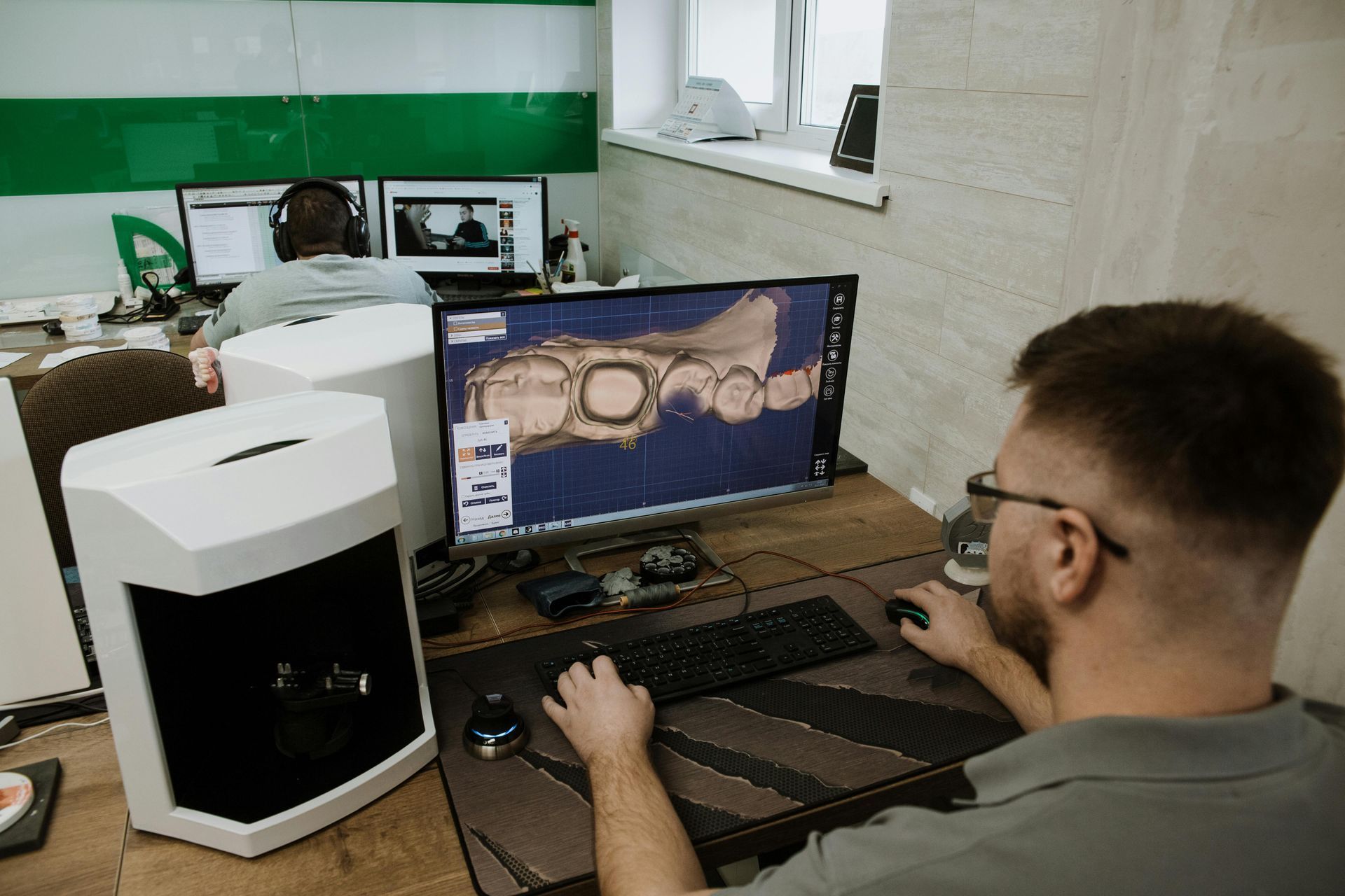 Man working at a desktop computer beside a large white PC tower in a lab or office setting