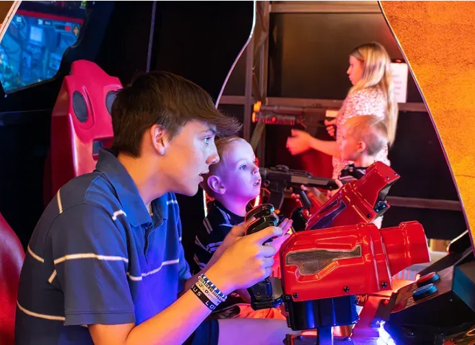 A boy and two children are playing a video game in an arcade.