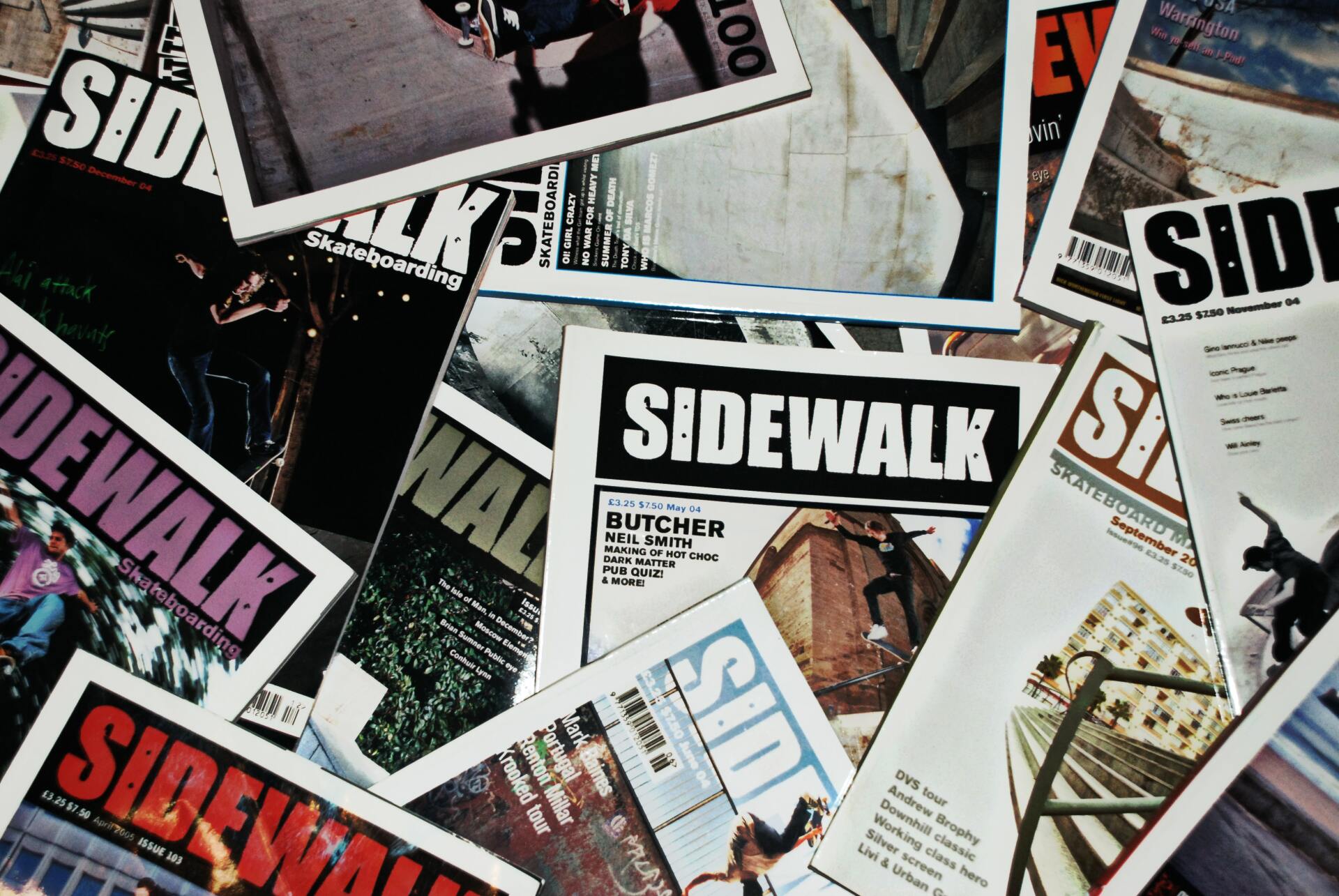 A pile of sidewalk magazines are stacked on top of each other