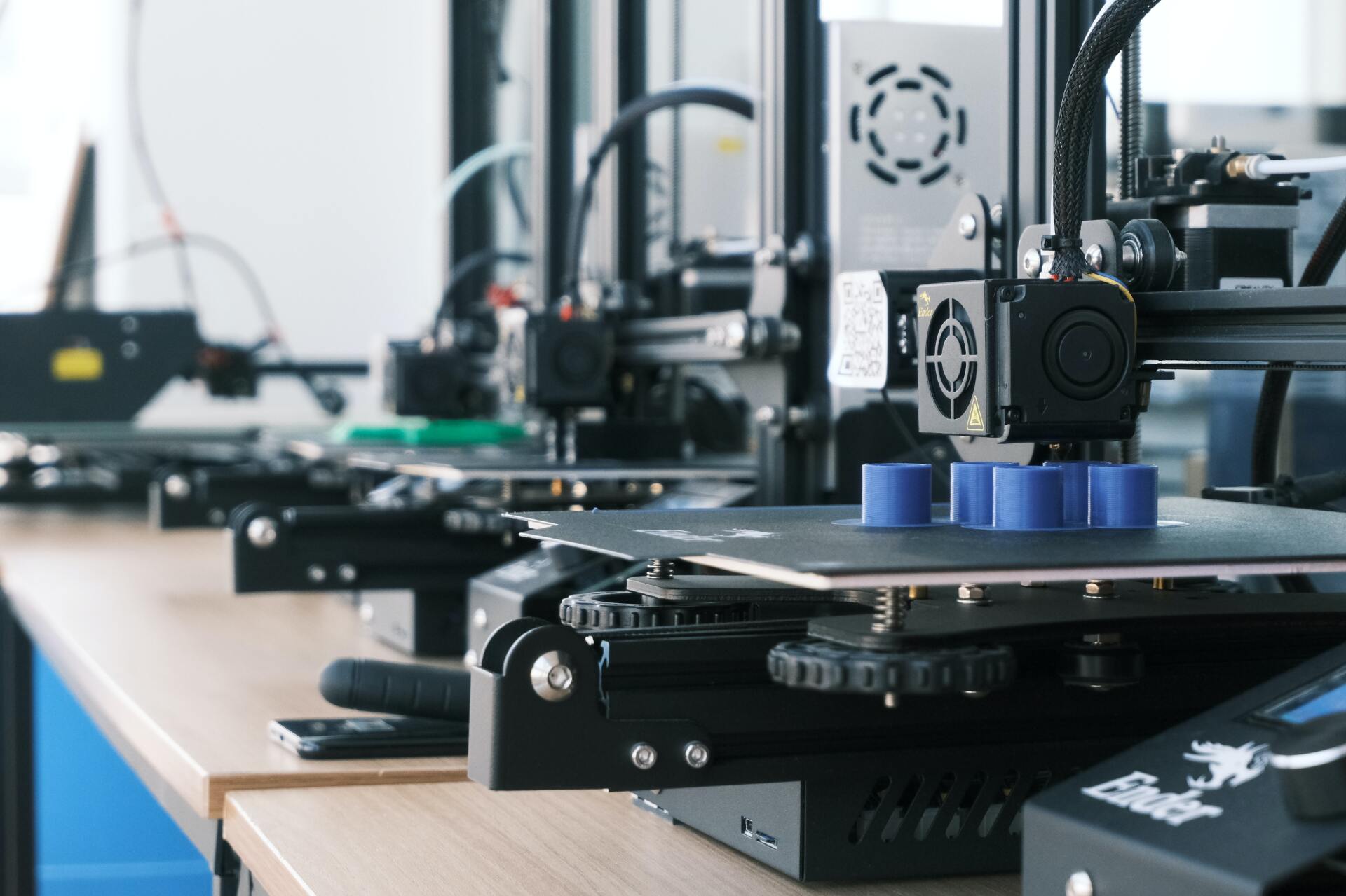 A row of 3d printers are sitting on top of a wooden table.