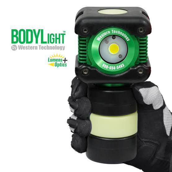 Handheld black-and-green BODYlight flashlight with glowing circular lamp, held in a gloved hand