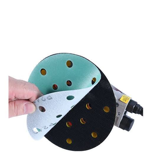 Hand holding a peeled-back sanding disc showing layered abrasive pads in teal, white, and black with perforations