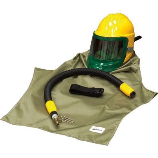 Yellow firefighter helmet with green face shield, gloves, hose, and protective hood on a gray surface