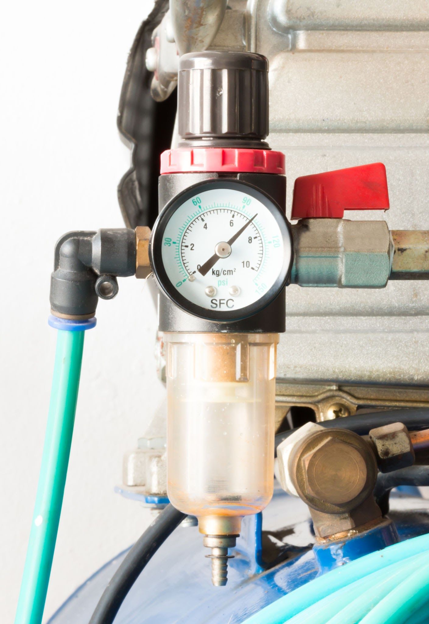 Air compressor regulator with pressure gauge, clear filter bowl, and attached hoses and valve.