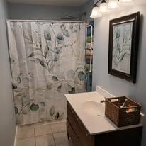 Small bathroom with leaf shower curtain, white vanity, mirror, and overhead lights.