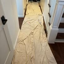 Beige fabric laid out on a hallway floor between white doorways and dark wood flooring