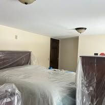 Bedroom with plastic-covered furniture and a doorway, suggesting a room being cleaned or moved into