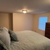 Bedroom with a large bed, beige walls, ceiling light, and a window with white blinds