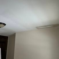 Empty room ceiling and beige wall with a light fixture and doorway visible