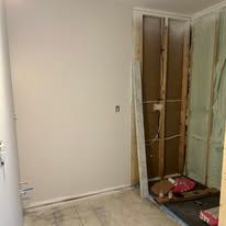 Damaged interior wall with exposed framing and debris in a room corner