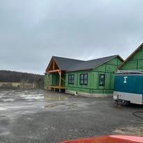 Green cabin building beside a trailer on a muddy lot under a gray sky