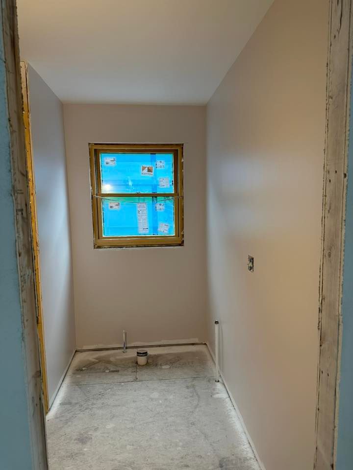 Narrow unfinished hallway with a small window and exposed drywall, showing a bare floor under renovation