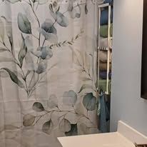 Shower curtain with gray-green leaf pattern beside a bathroom vanity and wall mirror