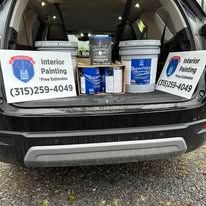 Open car trunk with Interior Painting signs, paint cans, and supplies inside.