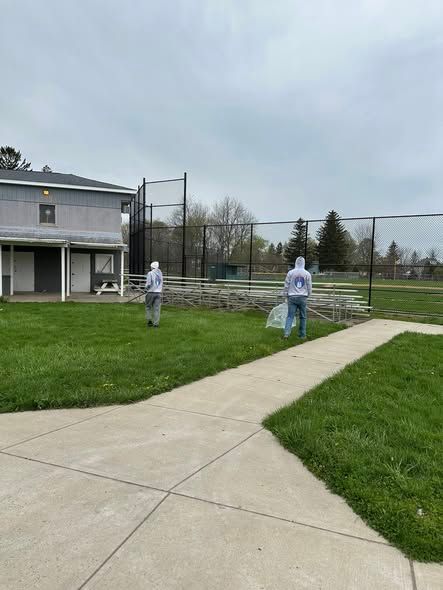 Two people in protective suits spraying a lawn beside a house and fenced yard
