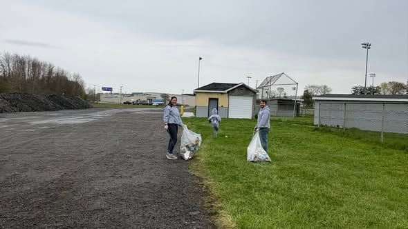 Three people picking up litter along a roadside near a grassy field