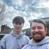 Two people smiling outdoors under a cloudy sky, one taking a selfie