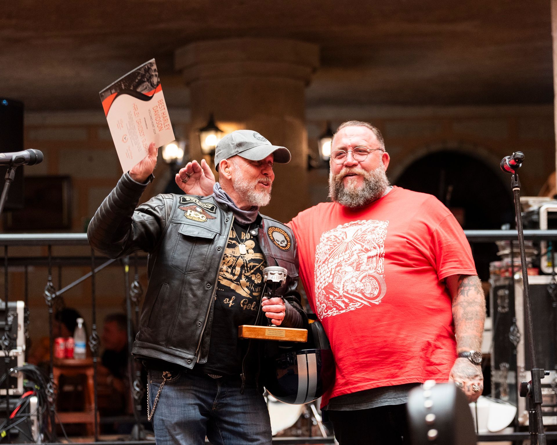 A man in a red shirt is standing next to a man in a leather jacket