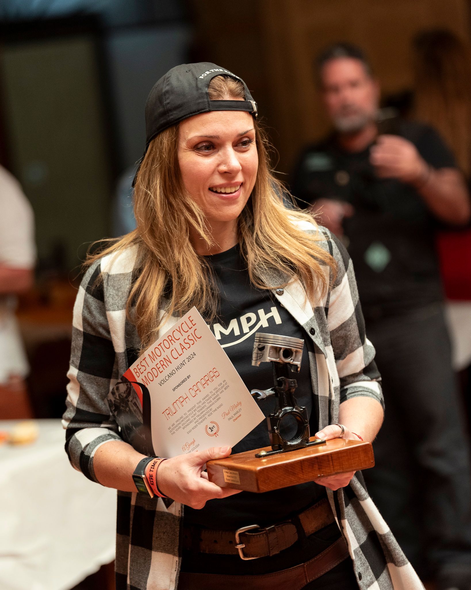 A woman in a plaid shirt is holding a trophy and a certificate.