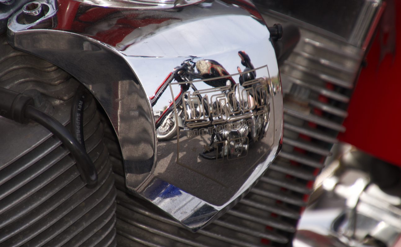 A close up of a motorcycle engine with a reflection of a person riding a motorcycle