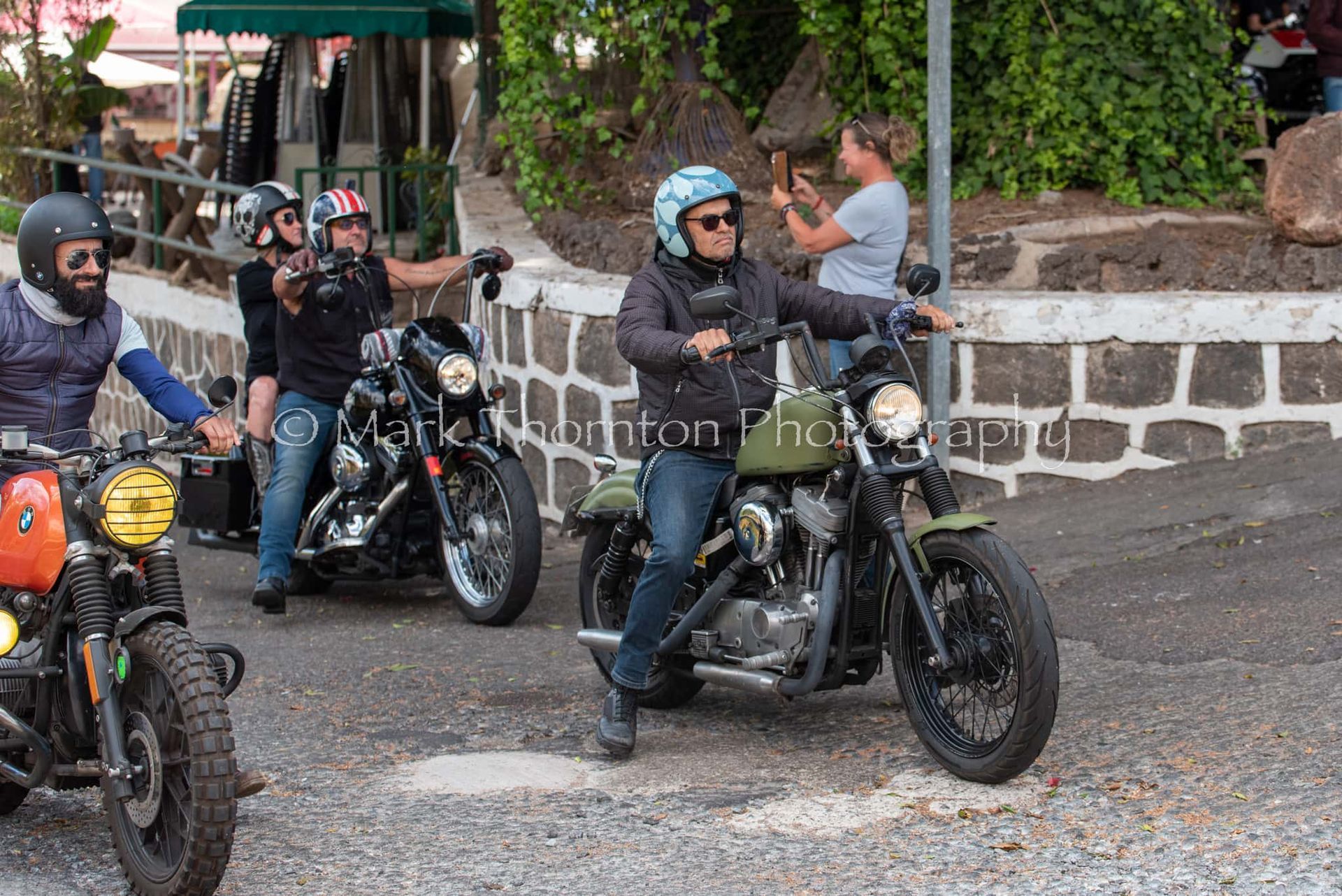 A group of men are riding motorcycles down a gravel road.