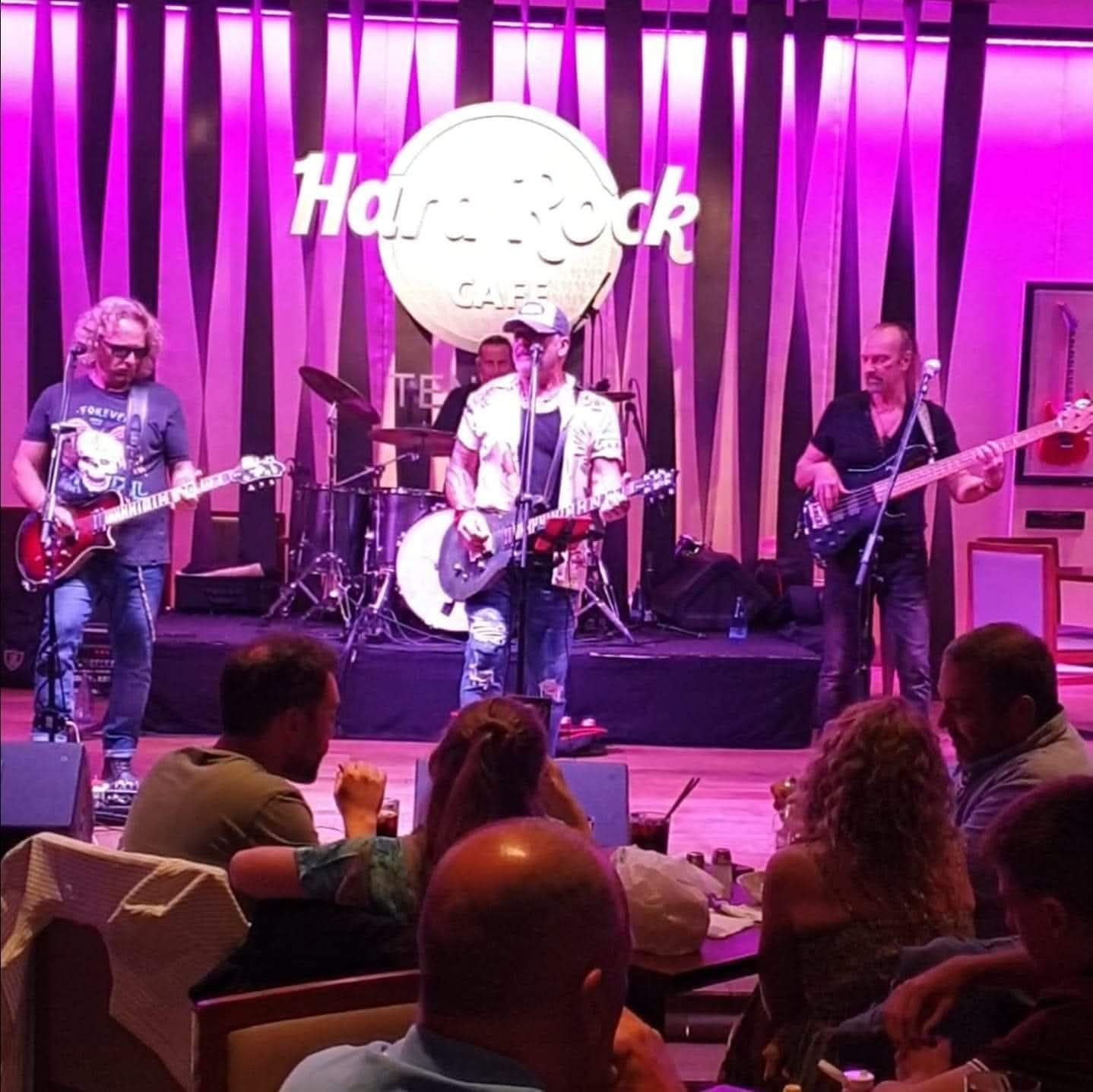 A group of people are sitting in front of a hard rock cafe sign