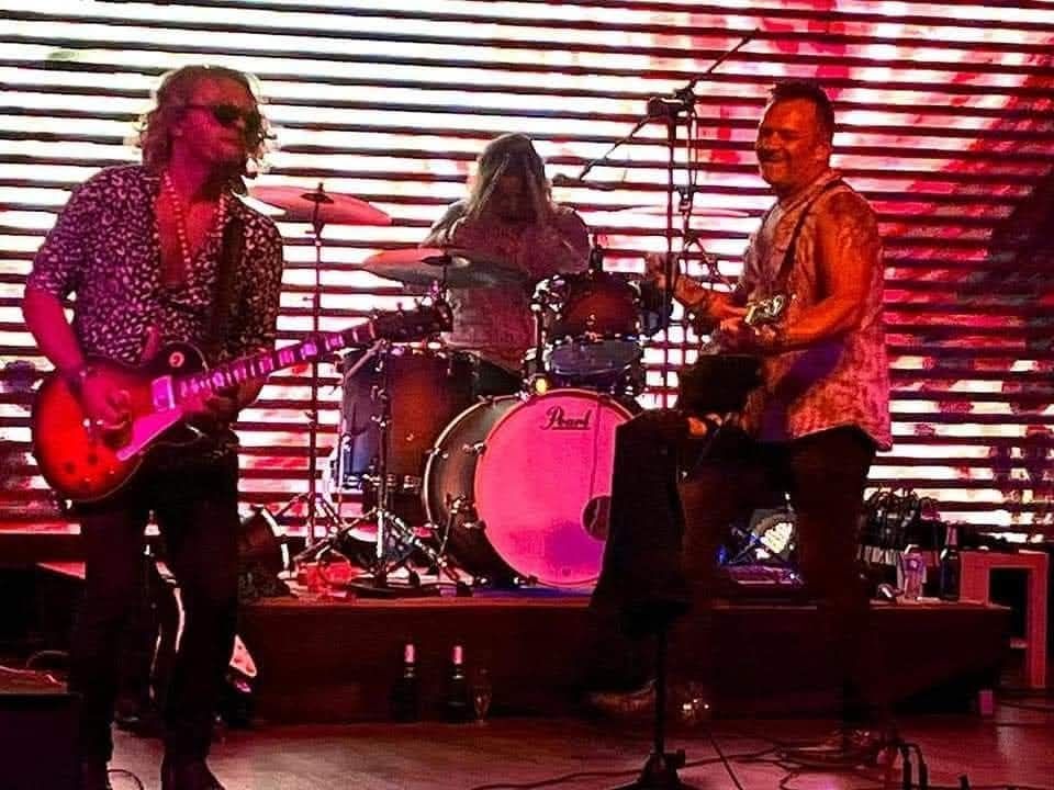 Three men are playing guitars and drums on a stage.