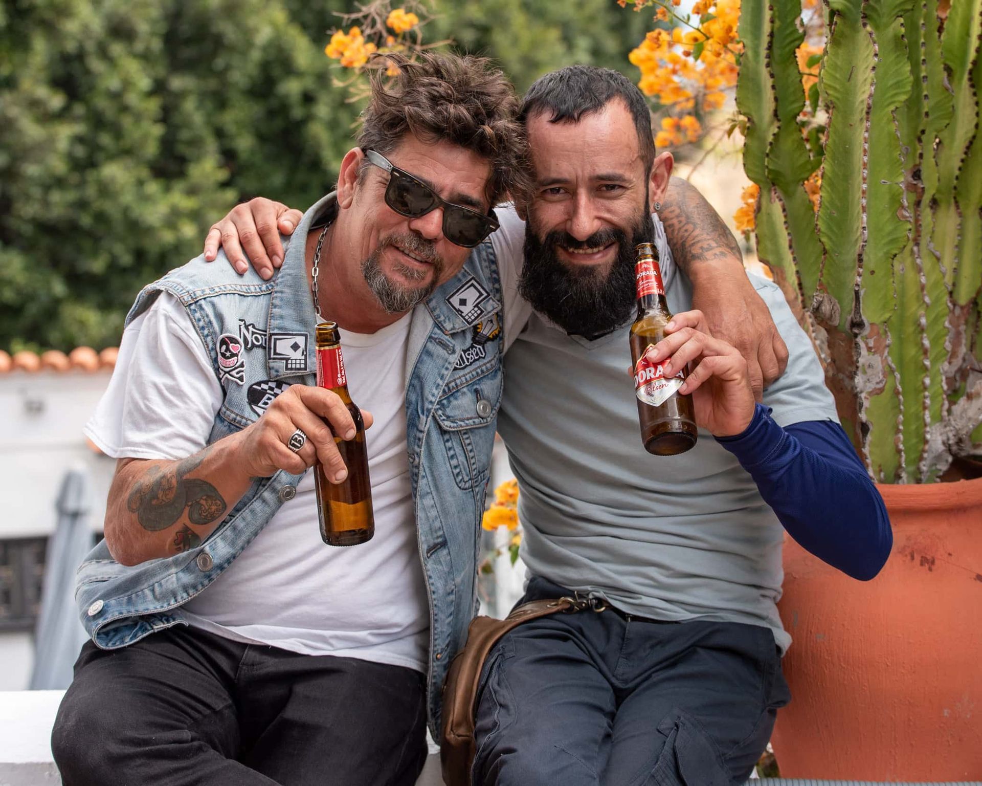 Two men are sitting next to each other holding bottles of beer.