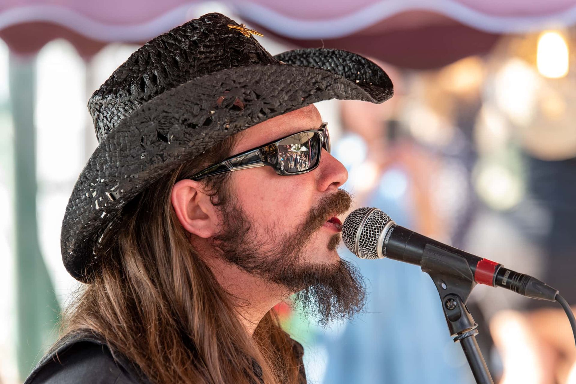 A man wearing a cowboy hat and sunglasses is singing into a microphone.
