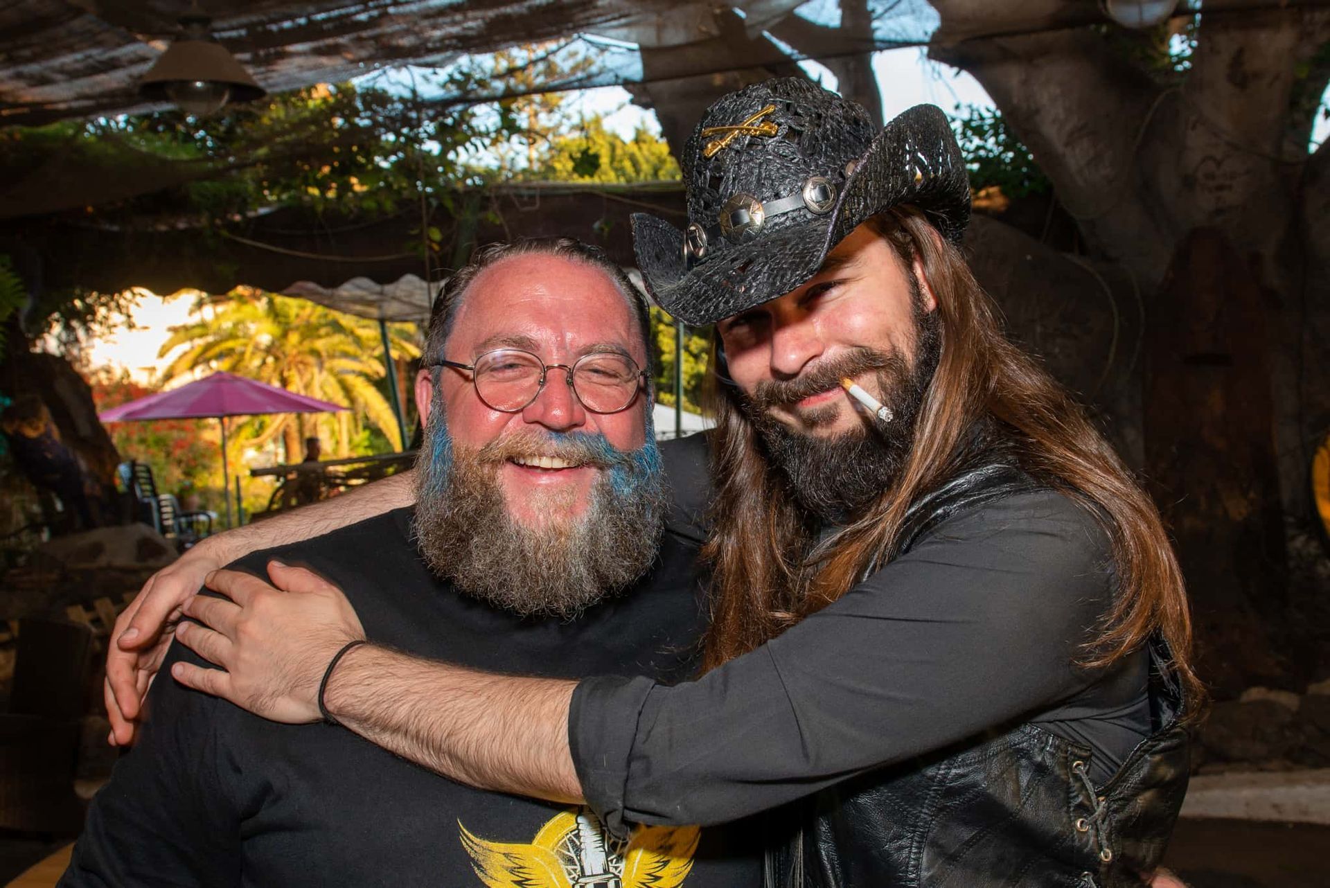 A man with a beard is hugging another man with long hair.