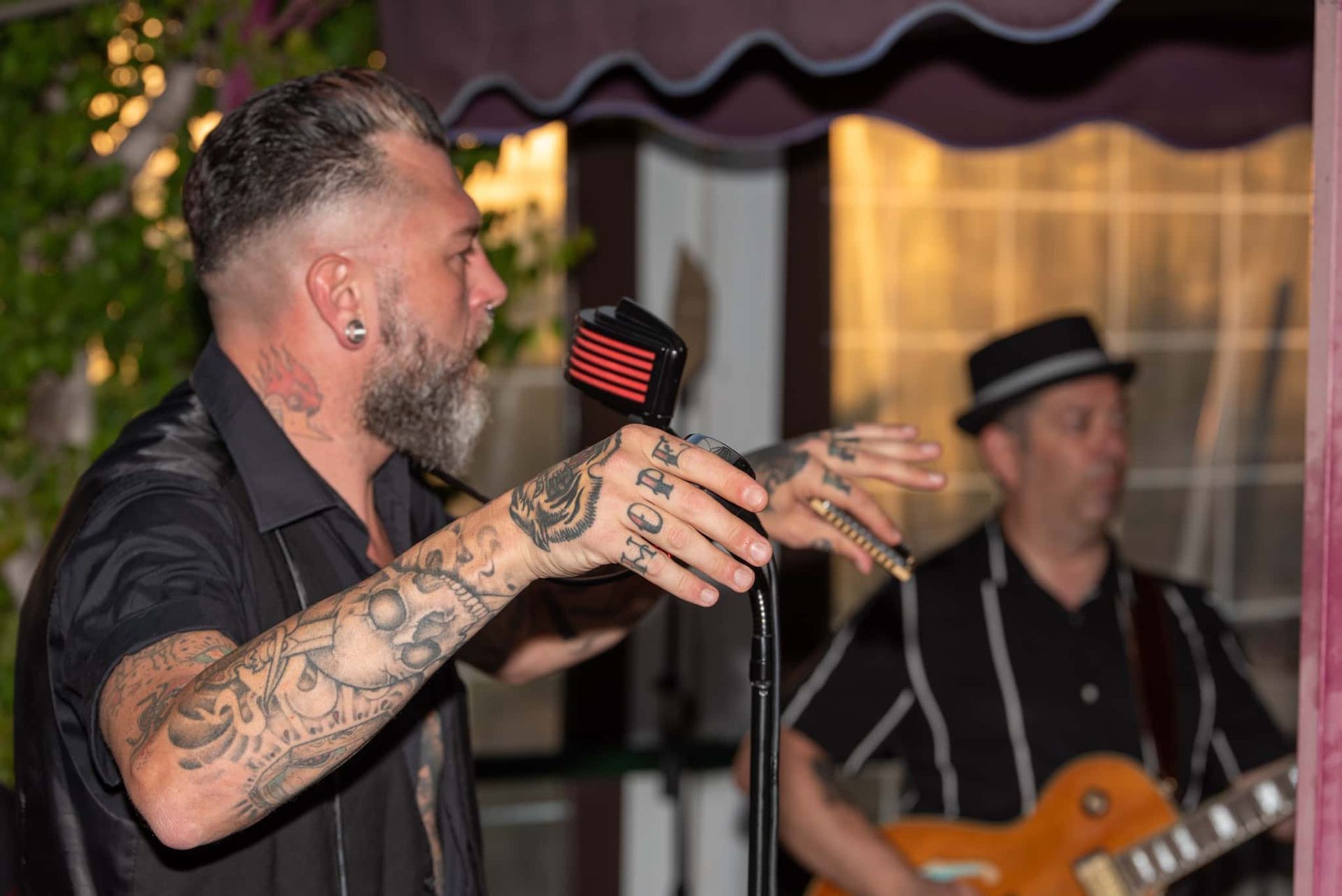 A man with tattoos is singing into a microphone while another man plays a guitar.