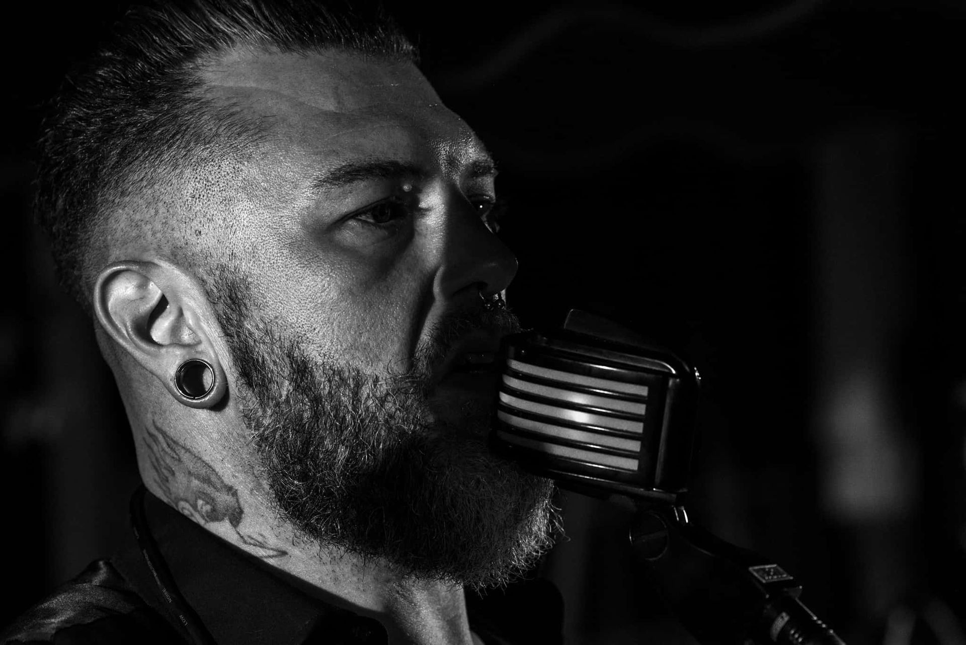 A man with a beard is singing into a microphone in a black and white photo.