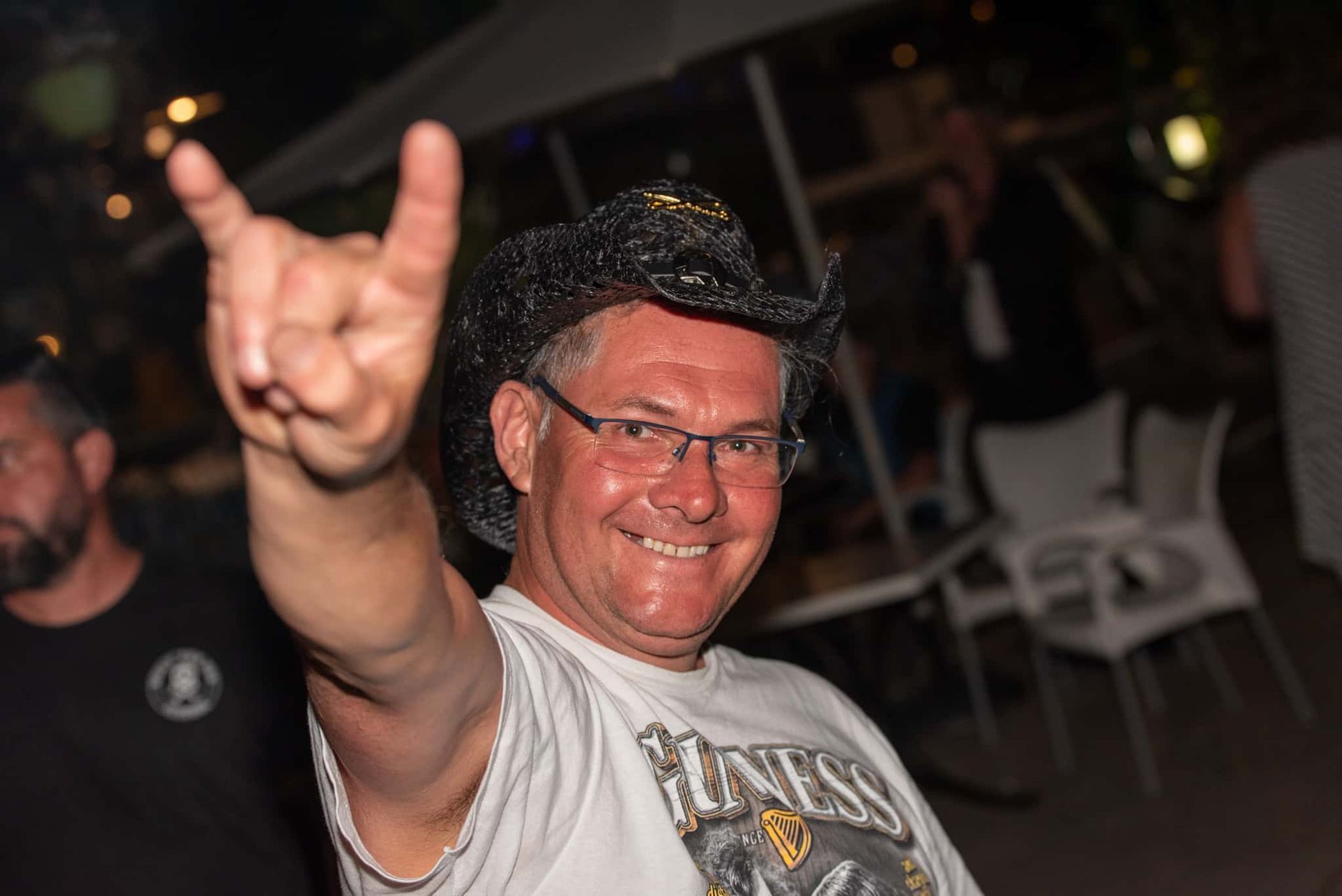 A man wearing a cowboy hat and glasses is giving the horns sign.