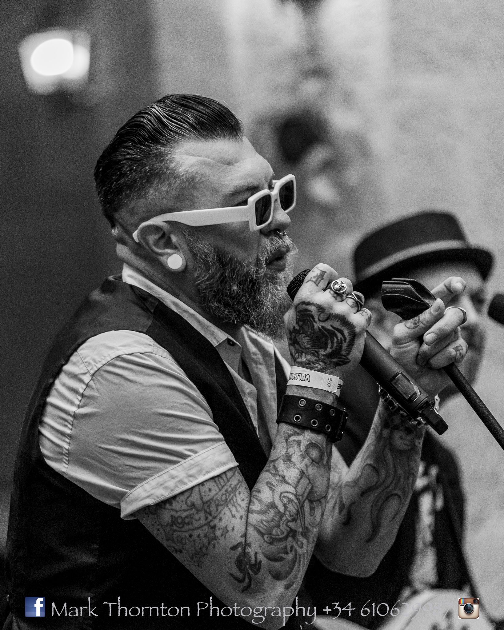 A man with a beard and sunglasses is singing into a microphone.