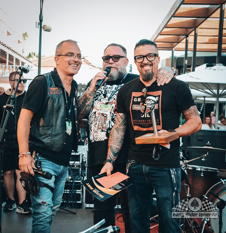 Three men standing next to each other with one wearing a t-shirt that says ' biker ' on it