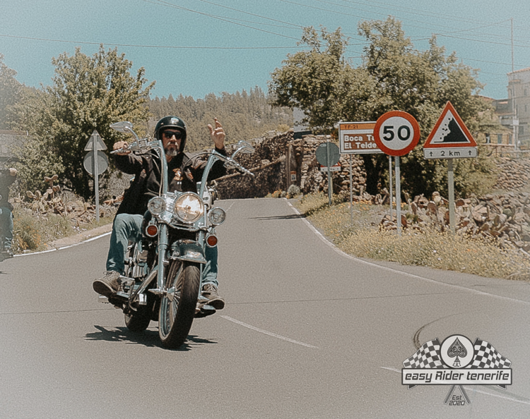 A man riding a motorcycle down a road with a 50 sign in the background