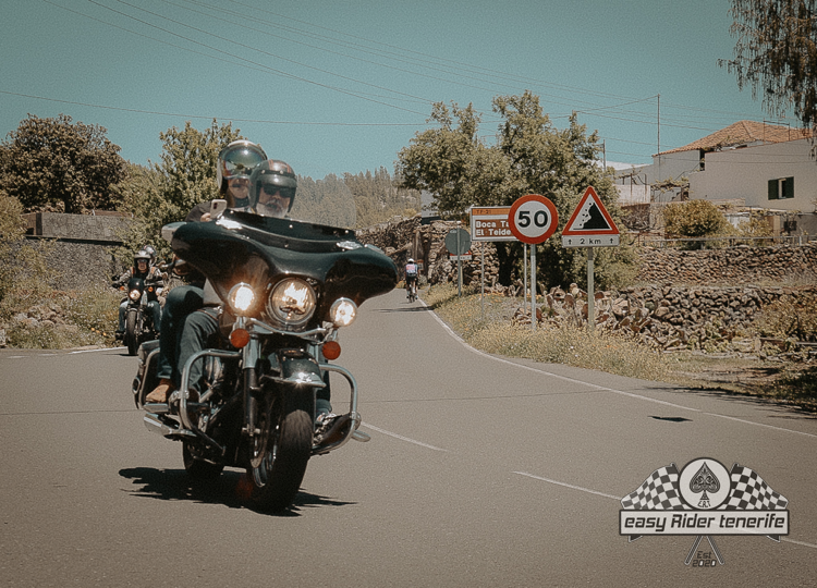 A man riding a motorcycle down a road with a 50 sign in the background