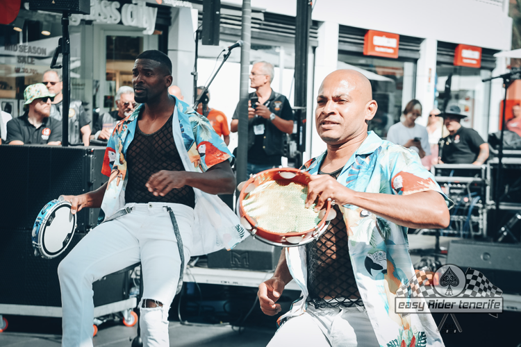 Two men are playing drums on a stage in front of a crowd.