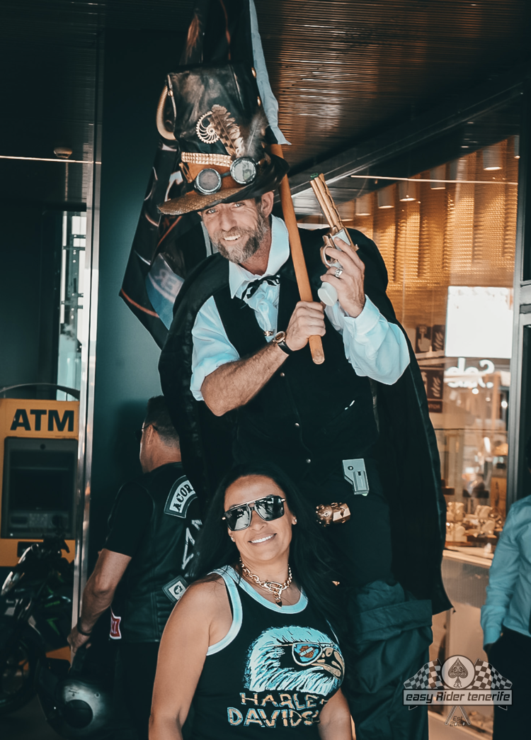 A man is standing on stilts next to a woman wearing a harley davidson shirt