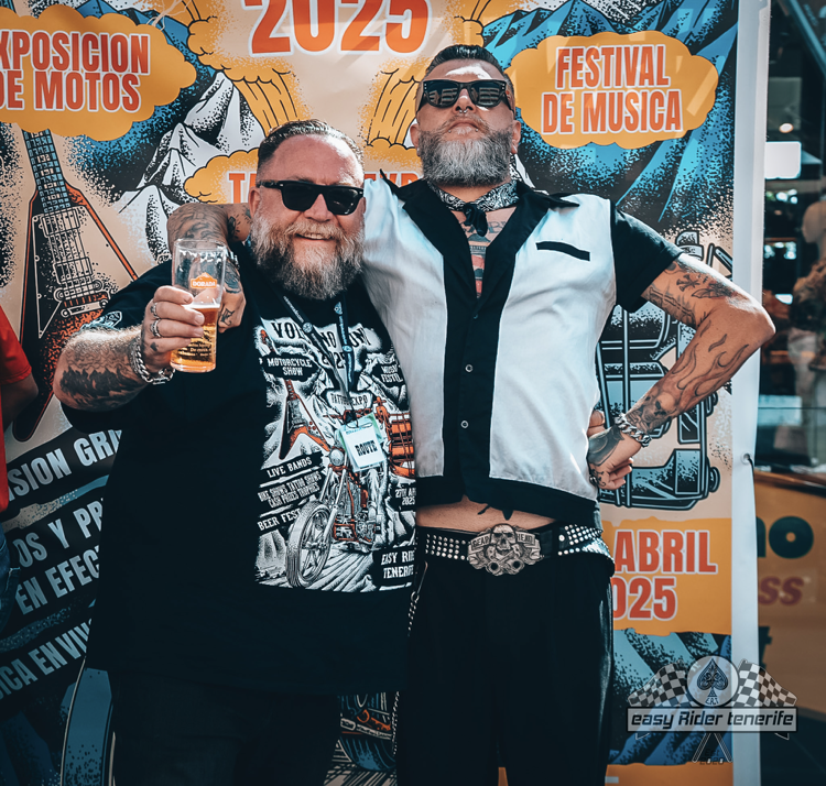 Two men are posing for a picture in front of a poster that says festival de musica