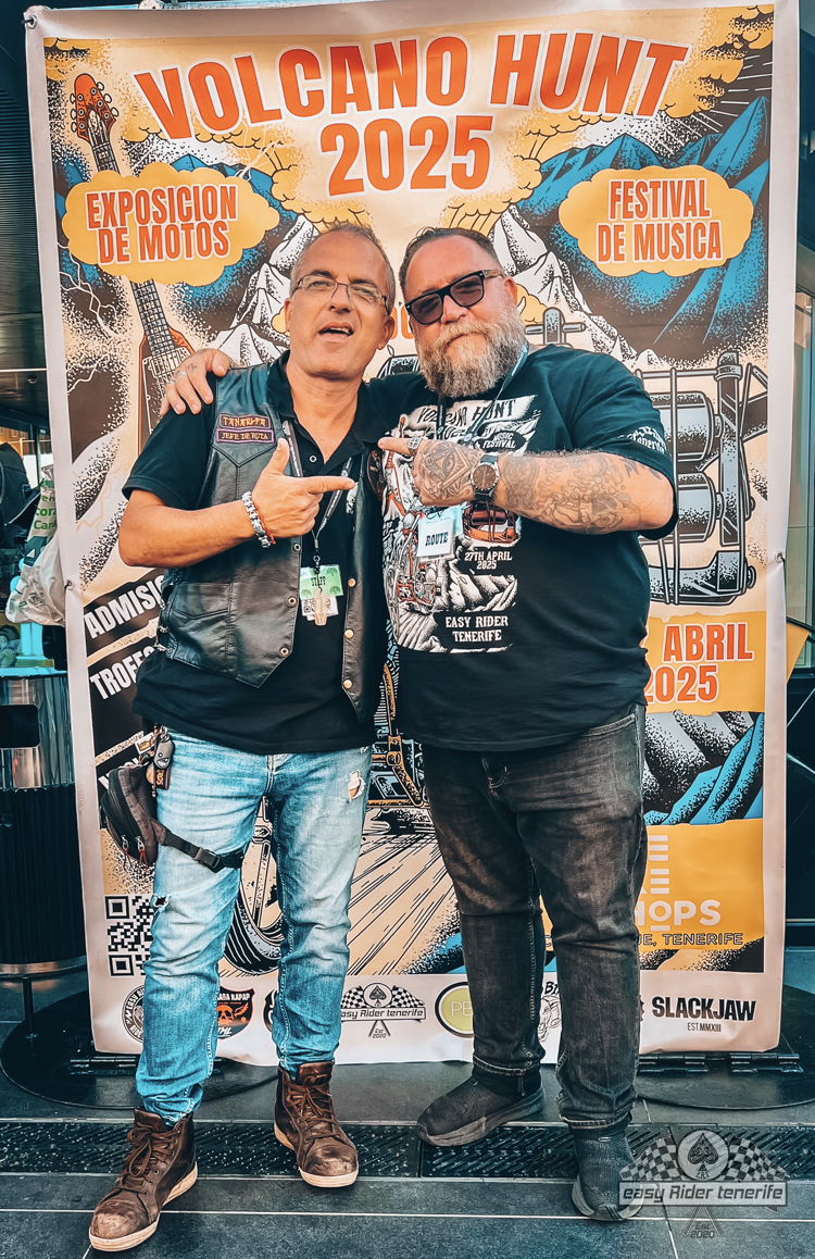 Two men are posing for a picture in front of a volcano hunt poster.