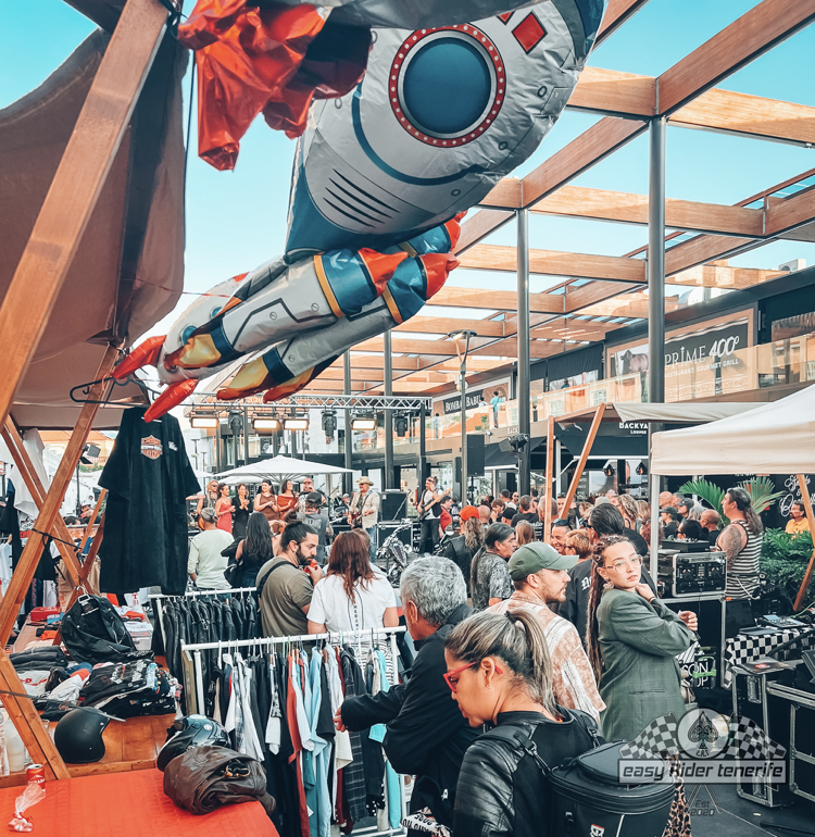 A crowd of people are gathered at a market with balloons hanging from the ceiling.