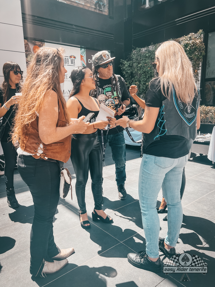 A group of women are standing next to each other on a sidewalk talking to each other.