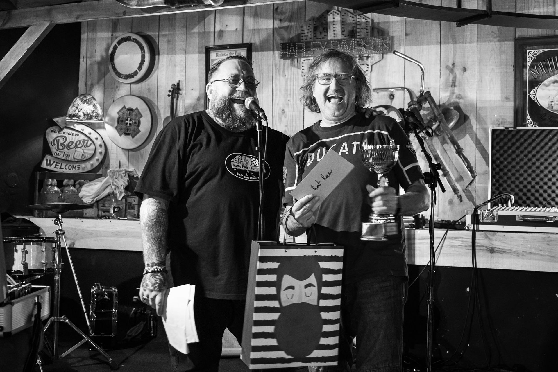 Two men are standing in front of a microphone in a black and white photo.