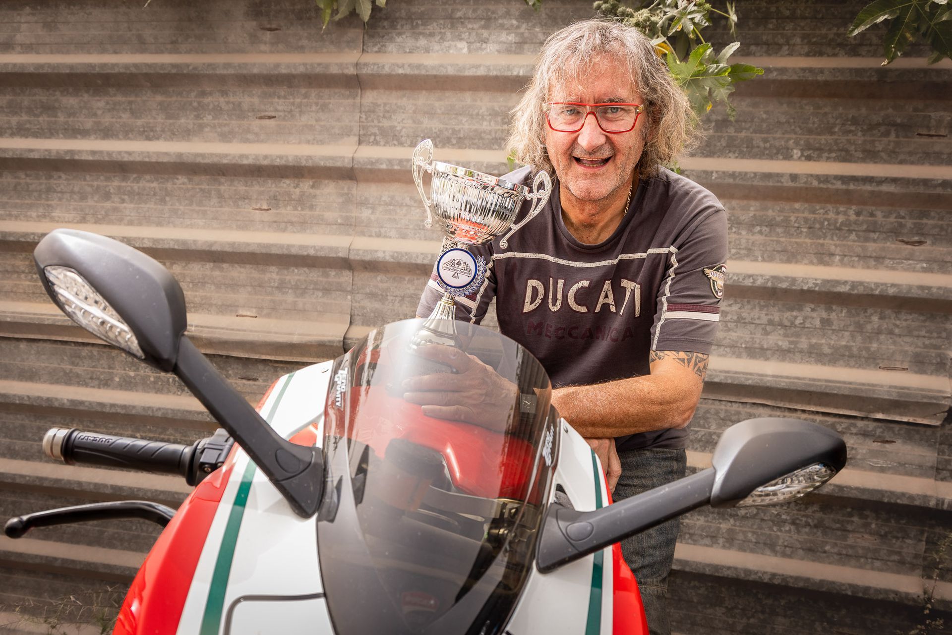 A man wearing a ducati shirt is standing next to a motorcycle.