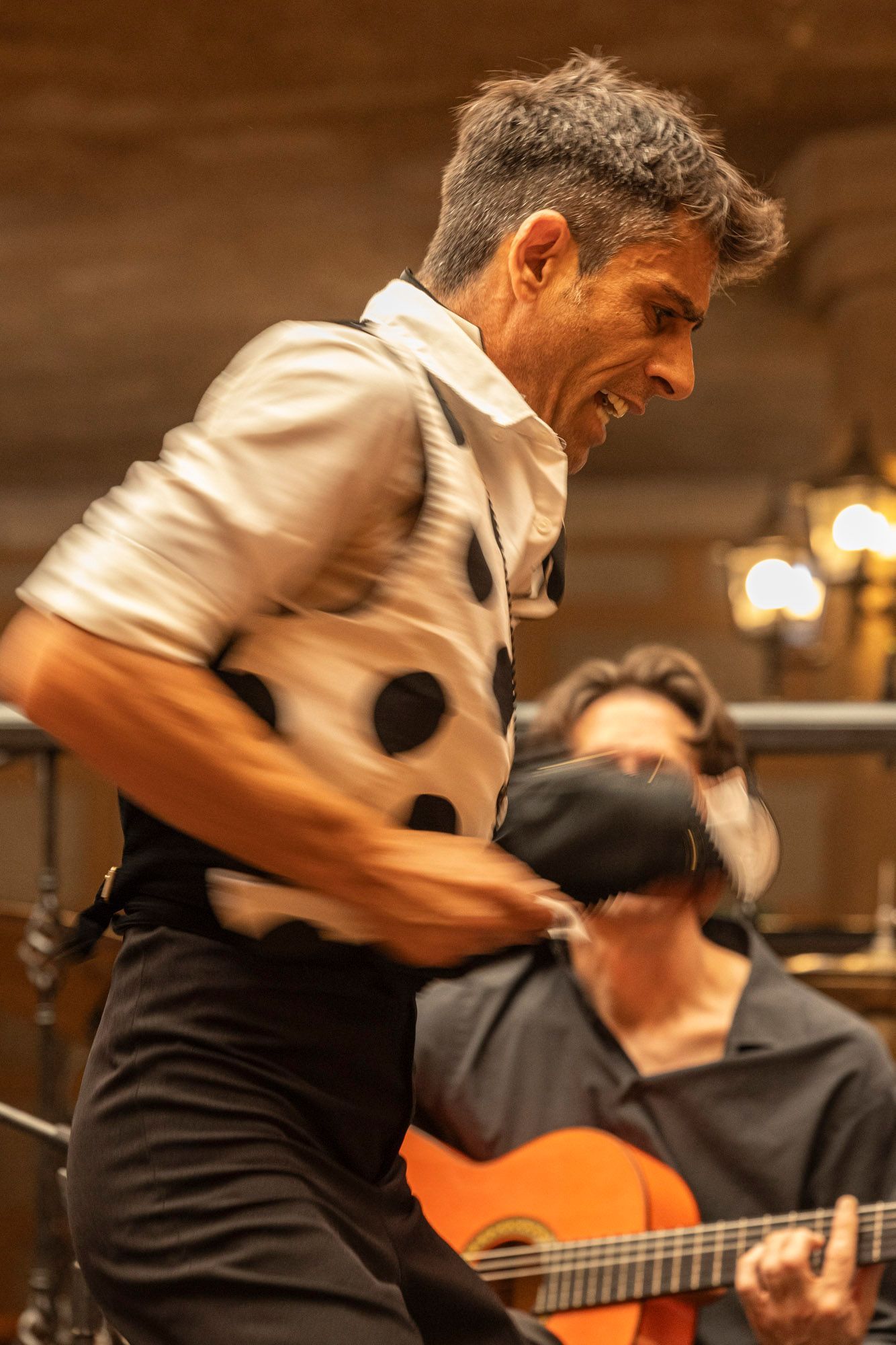 A man is playing a guitar while another man is dancing in the background.